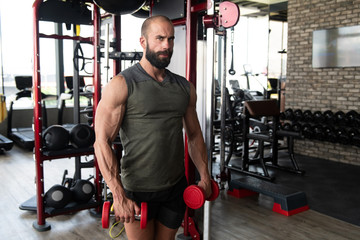 Fototapeta na wymiar Man In The Gym Exercising Shoulder With Dumbbells