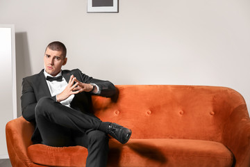 Handsome young man in elegant suit sitting on sofa indoors