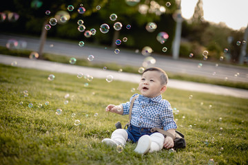 Baby boy wearing a bow tie and looking at bubbles in air sitting at the park