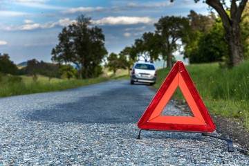 Red emergency stop sign and broken silver car on the road. Warning triangle on a country road in...