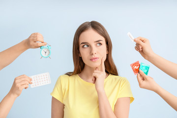Thoughtful young woman and hands with different means of contraception on color background