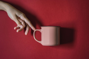 La creación de Adan, mano de mujer tocando una taza rosa en un fondo granate, michelangelo