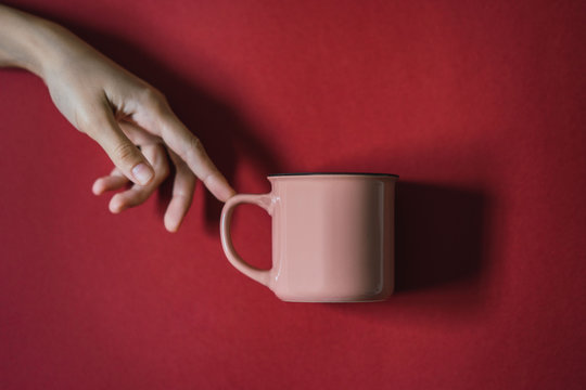 La creaci&oacute;n de Adan, mano de mujer tocando una taza rosa en un fondo granate, michelangelo