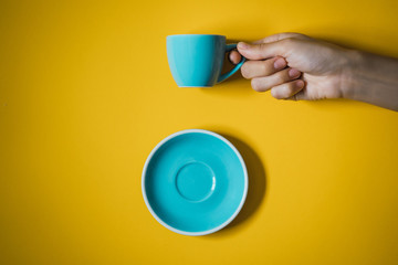 mano de mujer sujetando una taza de café con un plato debajo sobre un fondo amarillo