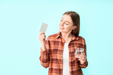 Young woman with birth control pills on color background