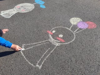 Kid drawing rain chasing dolls with a colourful sidewalk chalk 