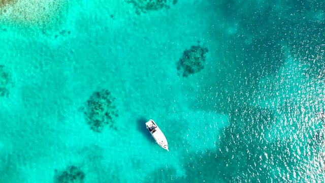 Aerial top down view of boat moving in open sea with clear and turquoise water on sunny day. Boat on  the tropical lagoon.