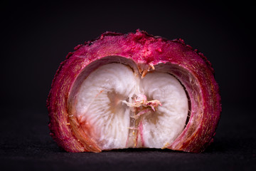 Half of a purplish-red exotic Mangosteen fruit showing the white flesh and revealing the thick...