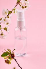 Obraz na płótnie Canvas bottle with transparent liquid. alcohol hand sanitizer over pink background with flower decoration.