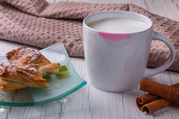 A Cup of coffee with a lipstick print on it. A bitten-off loaf on a plate.