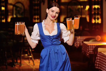 a sexy waiter girl with a big chest in Bavarian clothes holding a lot of beer mugs in the background of the bar during the celebration of the Oktoberfest