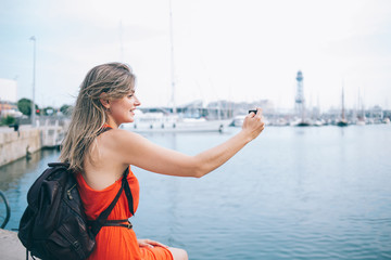 Fototapeta premium Uśmiechnięta podróżniczka biorąc selfie na smartfonie w nabrzeżu