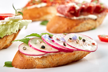 Assorted delicious bruschetta with tomatoes, strawberries, avocado, radish, Camembert and prosciutto. Close-up, top view, on a white background