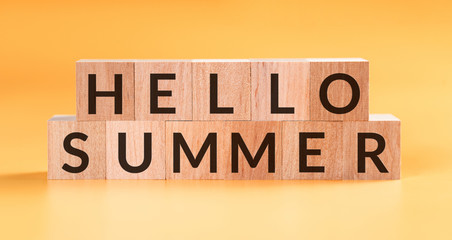 Hello Summer word written on wooden block on yellow background.