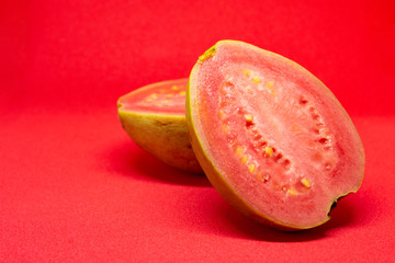 Pink guava cut in half on a pink background.