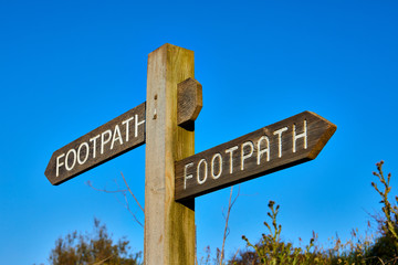 Image of a timber footpath sign with a clear blue sky, whth shallow sdepth of field, Selective focus.