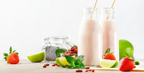 Healthy blended superfood drink. Organic diet smoothie with strawberry and goji berries, chia seeds and lime. Glass bottles with eco fendley straws. Gray background with copy space