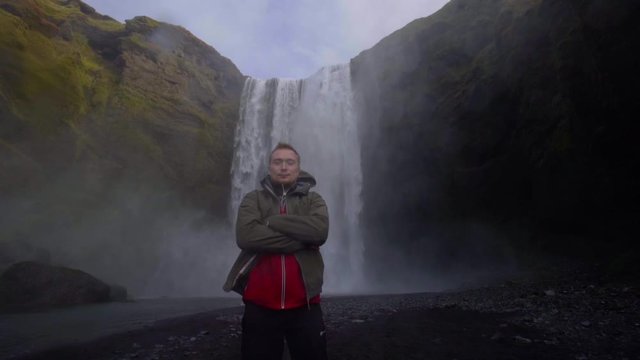 A guy poses in front of the backdrop of the huge Skogafoss waterfall