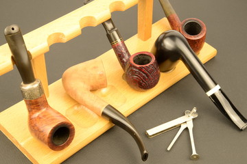 La bellezza della pipa: pipe da collezione dritte e curve di radica scura e chiara su supporto in legno chiaro e un reamers tamper, il tutto su fondo nero