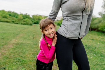 Little girl in sportswear looks out from behind mom
