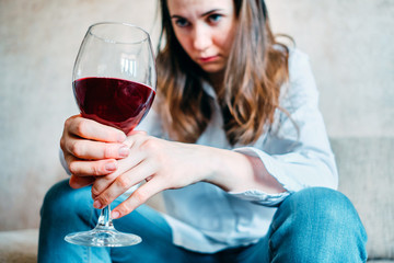 A drunk girl drinks wine and looks at a glass while sitting on a sofa.