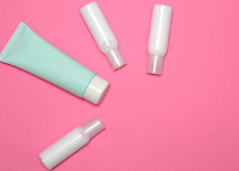 White cream tubes and one blue-green tube on light pink table. Care about face, hands, legs and body skin.
