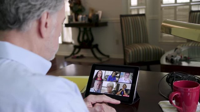 A team leader sitting in his living room holding a virtual meeting with team members due to the pandemic and the new reality in 2020 of working from home.