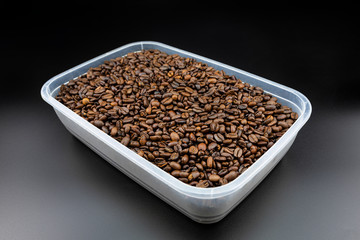 Fresh, roasted coffee beans in a plastic container, standing on a black table.

