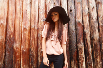 Beautiful girl in a black big hat on a background of a wall of wooden logs