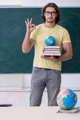 Young male geography teacher in front of blackboard