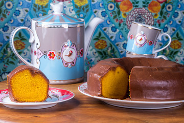 slice of carrot cake with chocolate sauce with teapot and cup of tea on patterned background