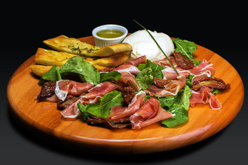 wooden cutting board with cheese burrata, ciabatta bread, ham, sausage,arugula e dried tomatoes. On...