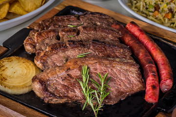 Picanha, a traditional cut of Brazilian meat, served with grilled onion and sausage on a hot iron plate. Served on hot iron plate. Close up