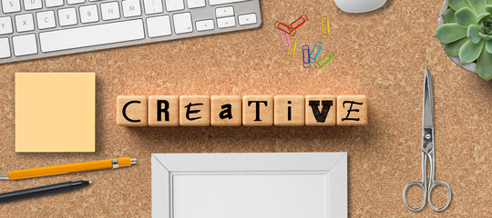 cubes with the word CREATIVITY and office items on cork background