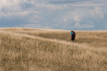A lone man hiking through native grasslands on the Saskatchewan prairie on a summer day.
