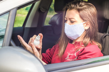 girl in medical mask in car treating her hands with disinfectant, sanitizer. woman using personal...