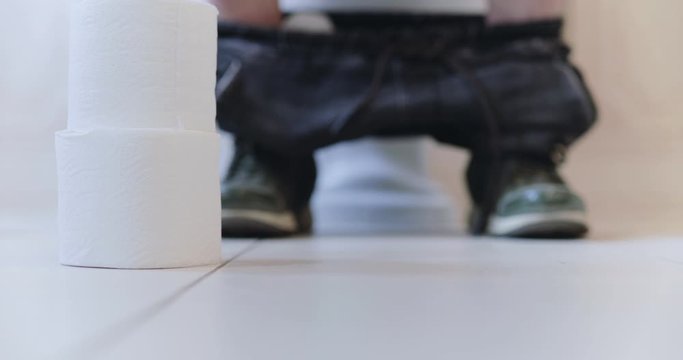 Coils of toilet paper on blurred background with male legs sits on lavatory pan