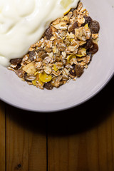 Muesli and yogurt in a white tile cup on a wooden table