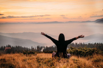  Yoga woman sitting on top of a mountain at sunrise. Mountains in the fog. The view from the back....