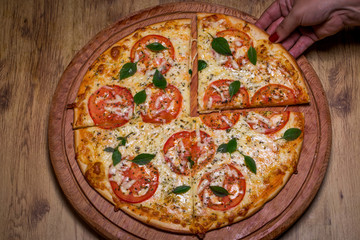 hand holding Margherita pizza on wooden background