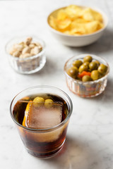 Appetizer consisting of red vermouth, olives, pistachios and chips. Marble table