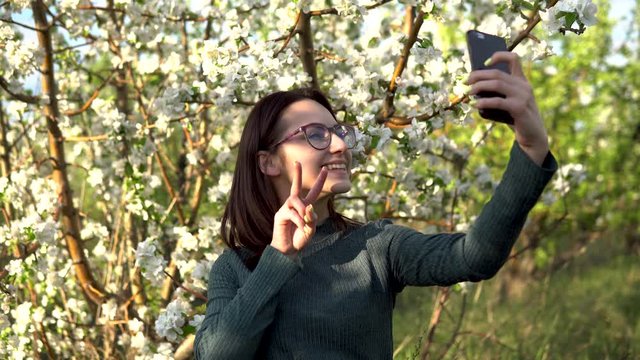 A young woman photographs herself against the backdrop of an apple tree. Girl in the blooming garden.