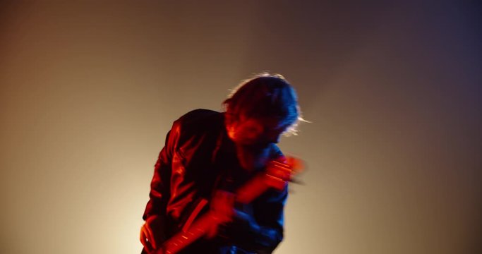 An amazing rock music player performing. Grunge musician is playing rock on bass guitar on stage, making a cool solo in red and blue neon lights 4k footage