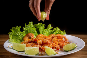 hand putting lemon on portion of shrimp fried in garlic and oil on wooden background