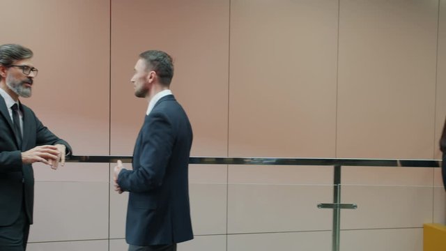 Male and female office workers in formalwear are talking in business center lobby standing in groups. Discussions, communication and people concept.