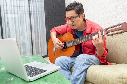 Man Looks Attentively At His Computer During A Virtual Guitar Lesson At Home