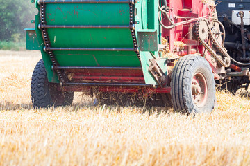 A tractor with a trailed bale making machine collects straw rolls in the field and makes round...