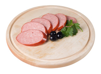 Raw smoked sausage, cut into slices on a board. Near olives and parsley