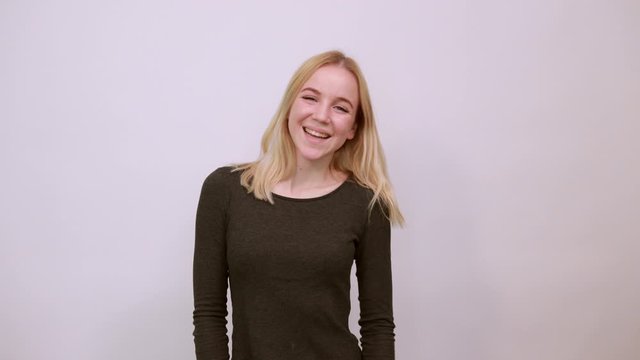 Young Blonde Woman In Black Sweater With Stylish Watch On White Background, Silly Girl Having Fun, Showing Two Fingers At Eye, Sticking Out Tongue. The Concept Of Cheerful, Funny And Carefree People