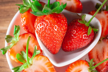 large fresh red strawberries with green stem on white ceramic plates with many slices of strawberries around © Wilson